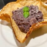 A creamy purple risotto is served in a golden crispy bread bowl, garnished with fresh green basil leaves, on a white plate.