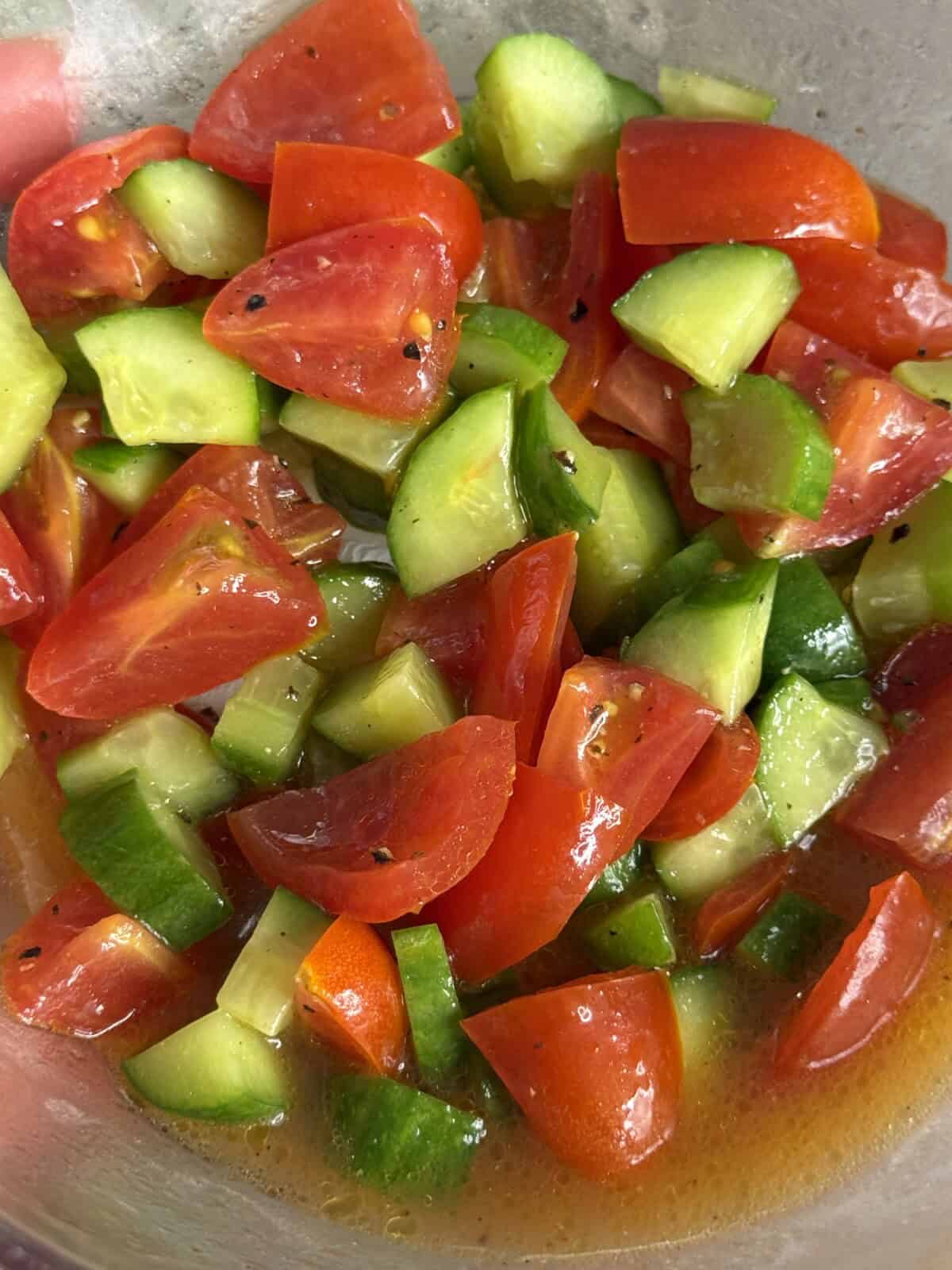 A close-up of a fresh salad with chopped tomatoes and cucumbers mixed in a light, seasoned dressing.