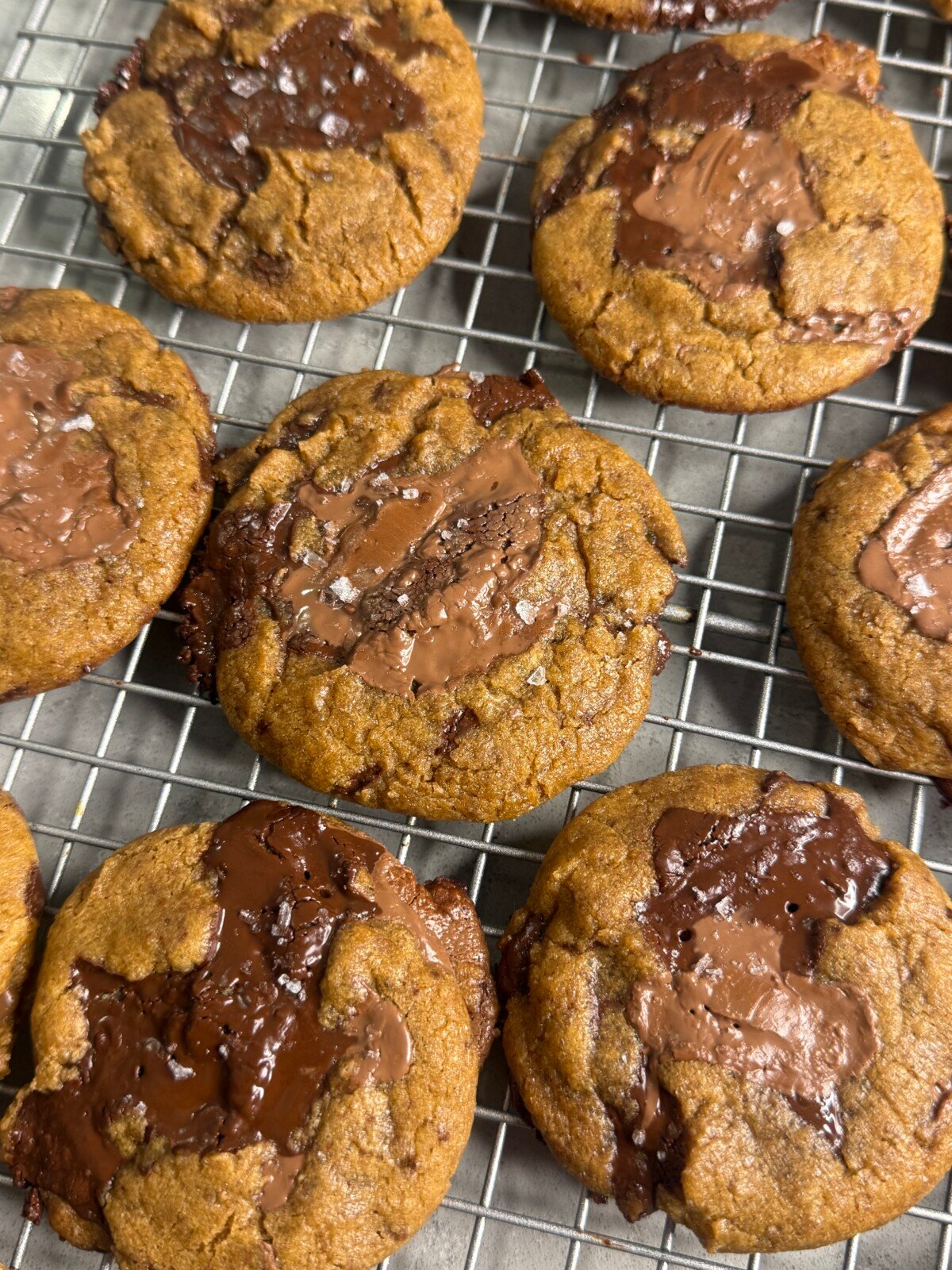 Freshly baked chocolate chip cookies with large melted chocolate chunks and a sprinkle of sea salt cooling on a wire rack.