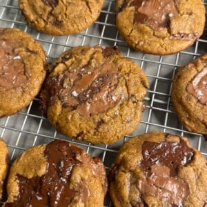 Freshly baked chocolate chip cookies with large melted chocolate chunks and a sprinkle of sea salt cooling on a wire rack.