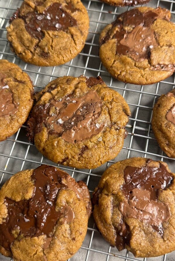 Freshly baked chocolate chip cookies with large melted chocolate chunks and a sprinkle of sea salt cooling on a wire rack.