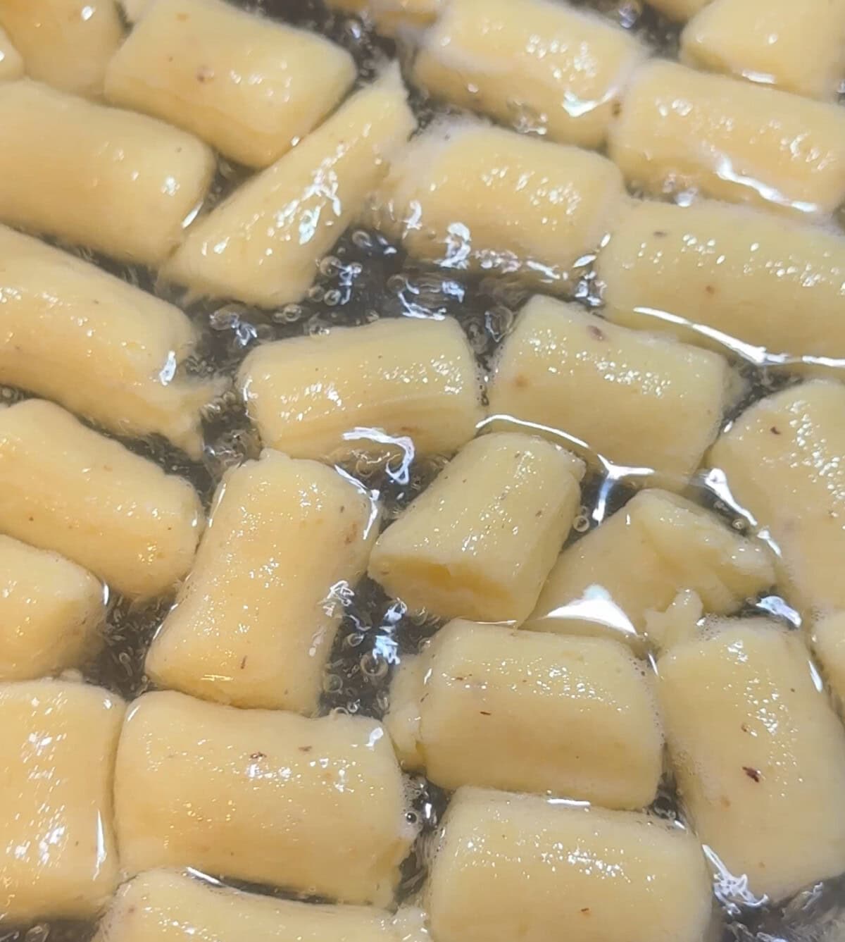 Short, uncooked gnocchi pieces are submerged in boiling water, with bubbles forming around them as they begin to cook.