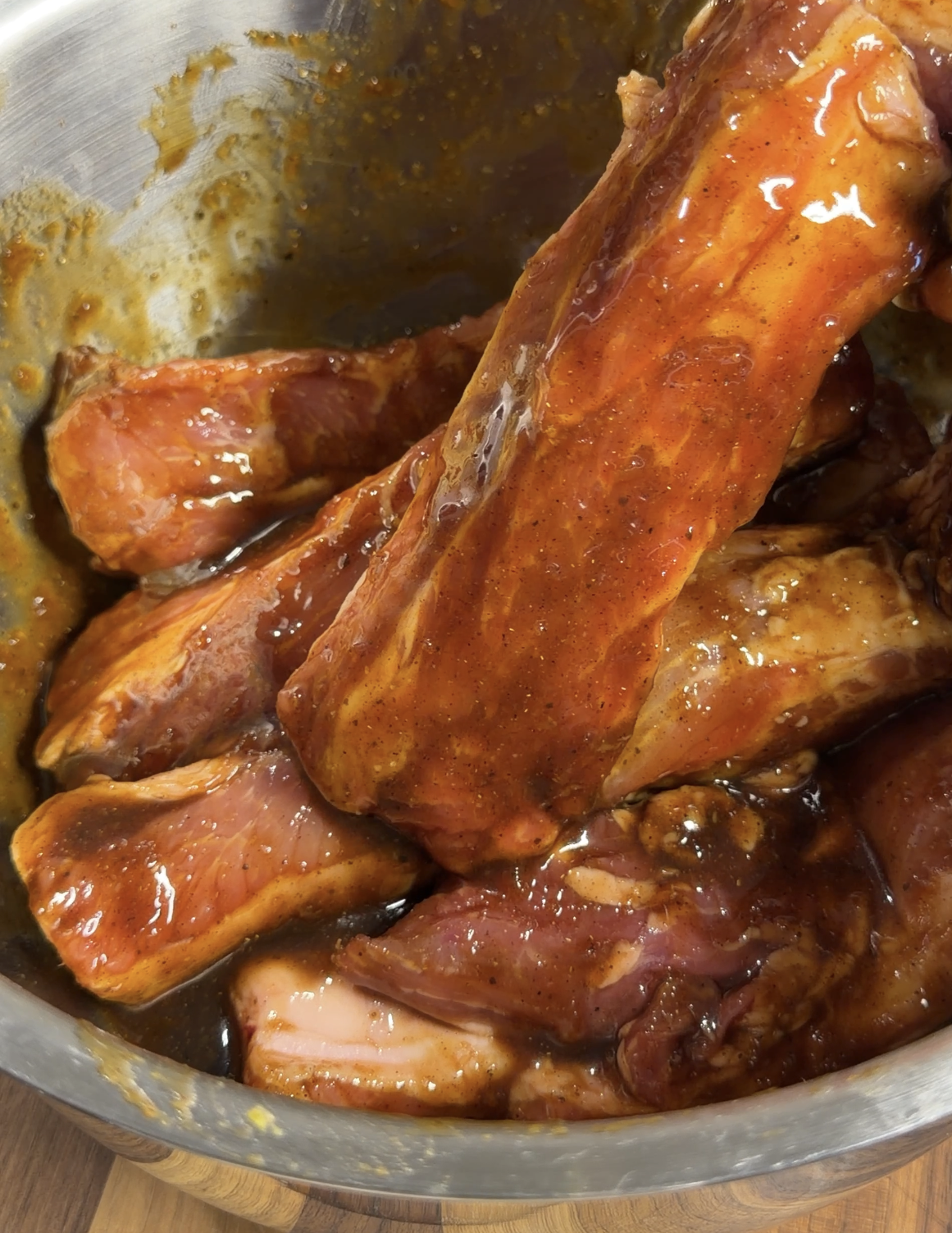 Raw pork ribs coated in a thick, reddish-brown marinade sit in a metal bowl, ready to be cooked.