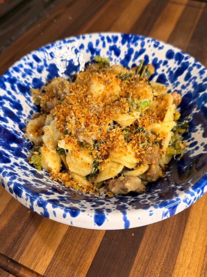 Orecchiette pasta with sausage and greens in a blue-and-white speckled bowl, topped with breadcrumbs.
