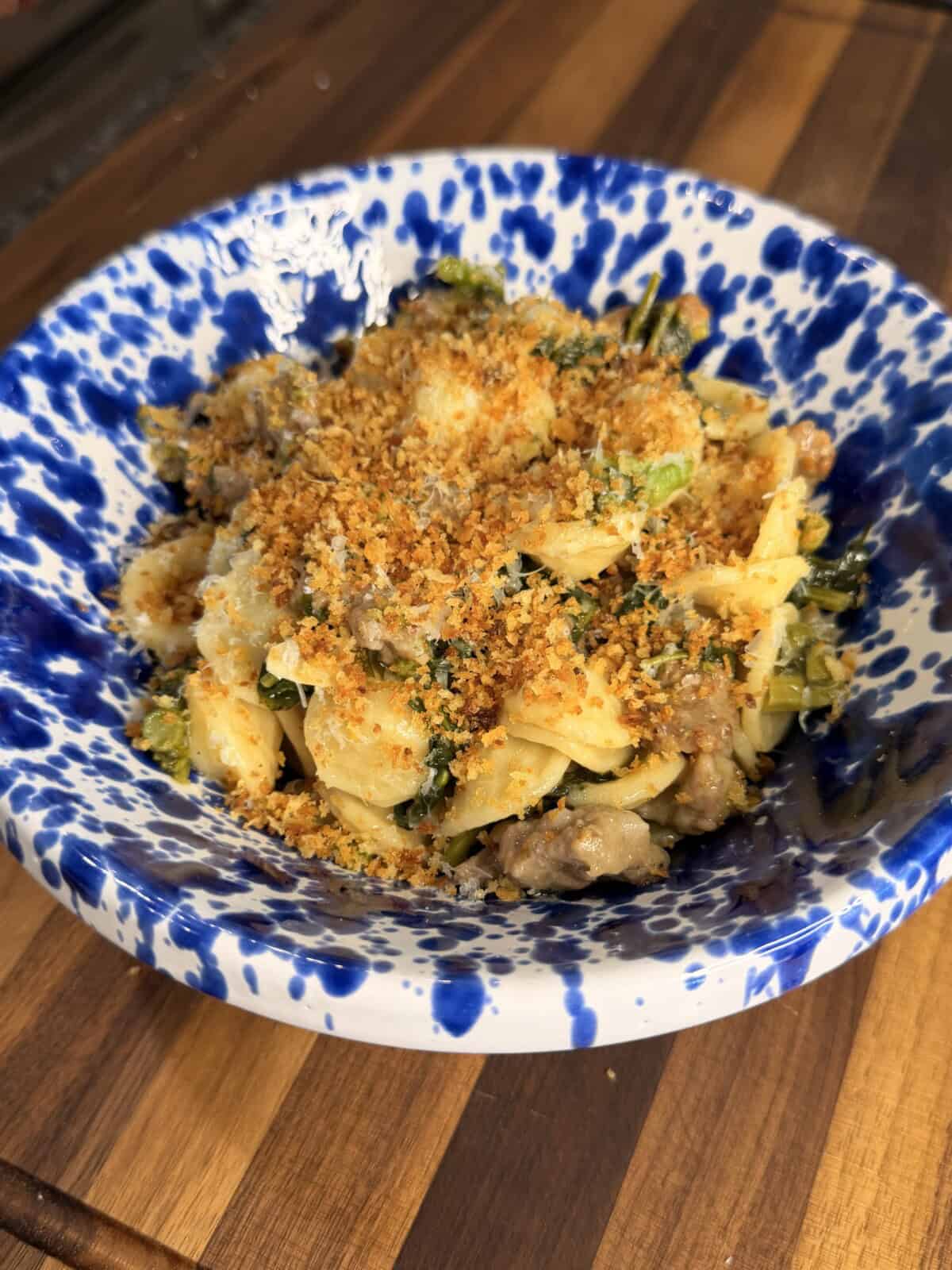 Orecchiette pasta with sausage and greens, topped with breadcrumbs in a blue and white splatter-pattern bowl.