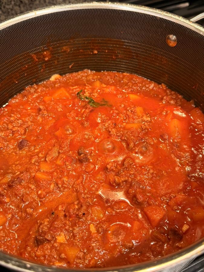 A pot of meat sauce simmering on a stovetop.
