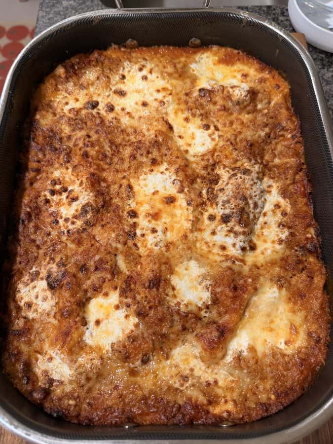 A rectangular metal baking dish filled with a baked lasagna topped with browned, bubbly cheese.