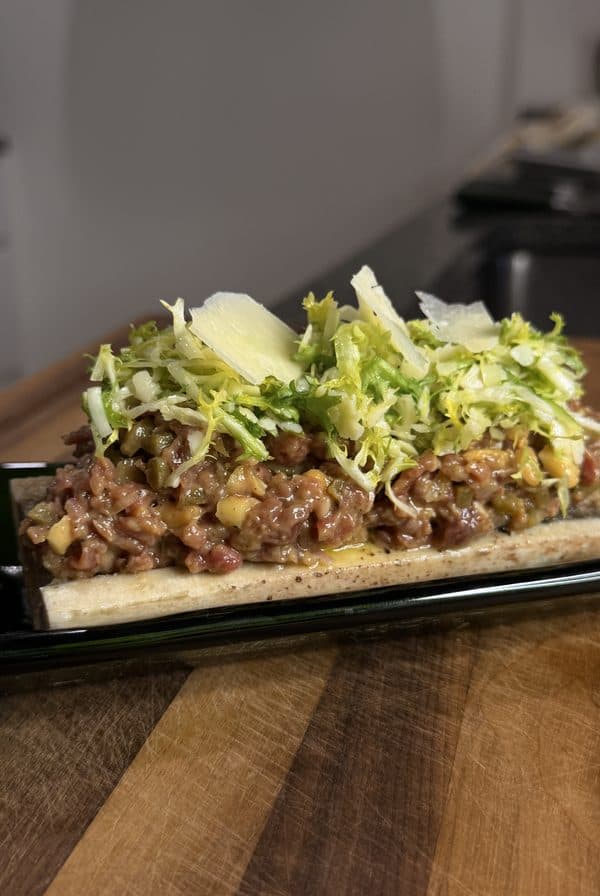 Beef tartare served on a roasted bone, topped with frisée and shaved parmesan.