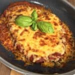 Chicken parmesan topped with melted cheese and fresh basil leaves in a nonstick skillet.
