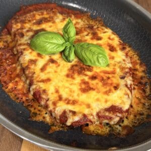 Chicken parmesan topped with melted cheese and fresh basil leaves in a nonstick skillet.