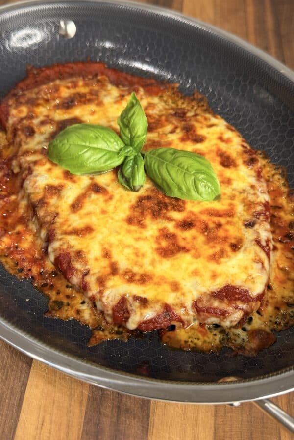 Chicken parmesan topped with melted cheese and fresh basil leaves in a nonstick skillet.