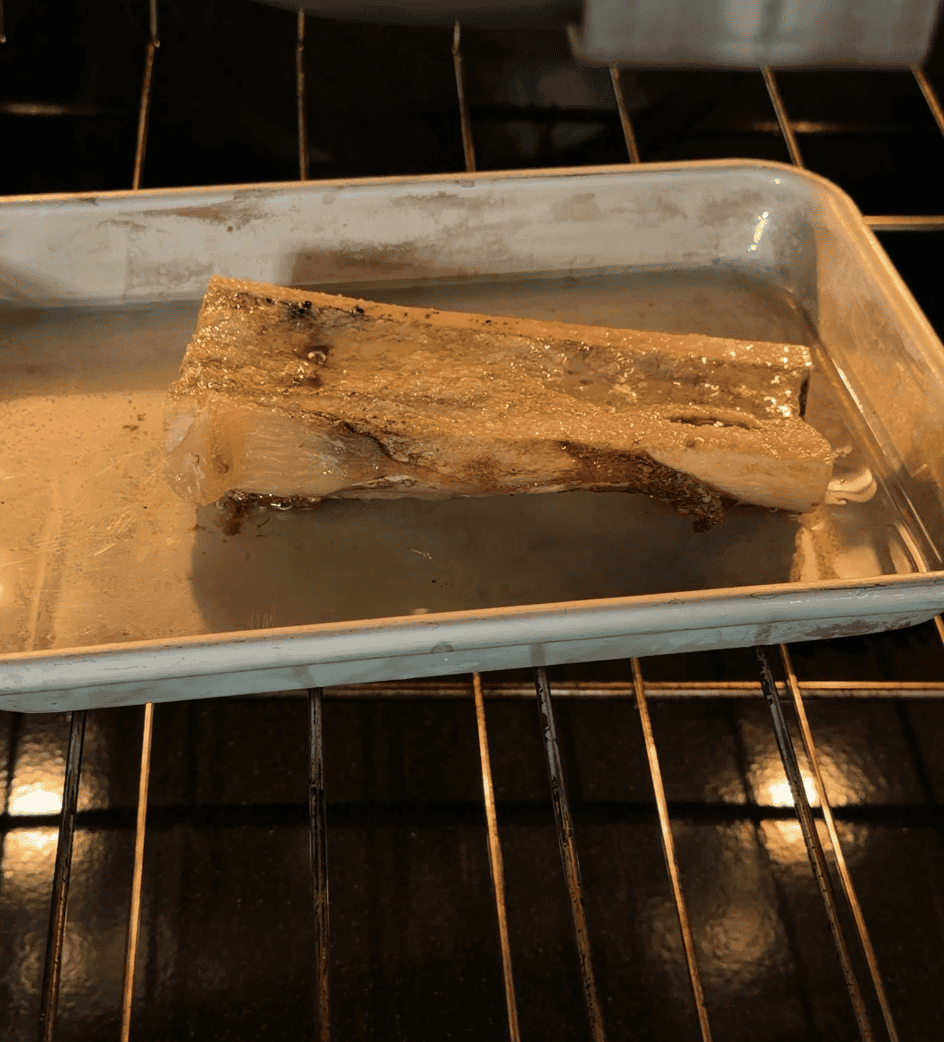 A marrow bone roasting on a metal tray inside an oven.